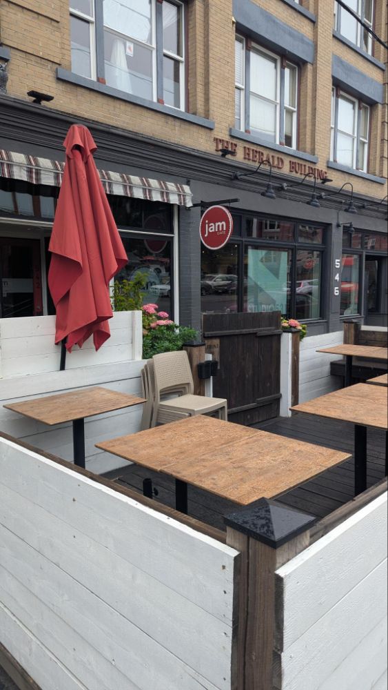 Photo of patio tables inside a white wooden fence, with a red sign for Jam in the background