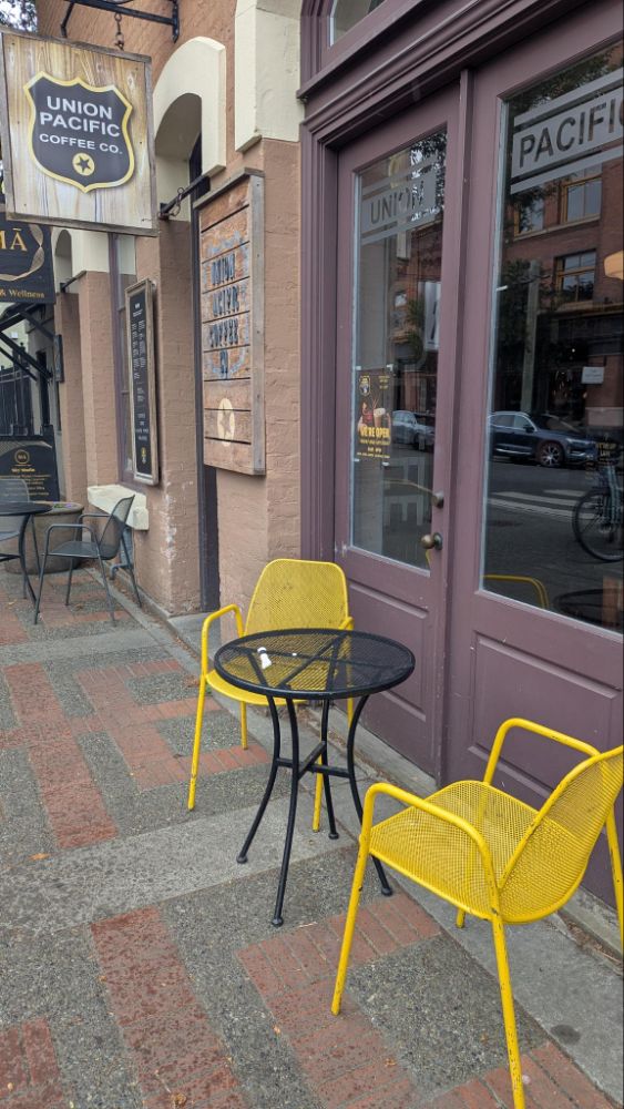 Photo of a patio with one round table and yellow chairs under a sign for Union Pacific Coffee