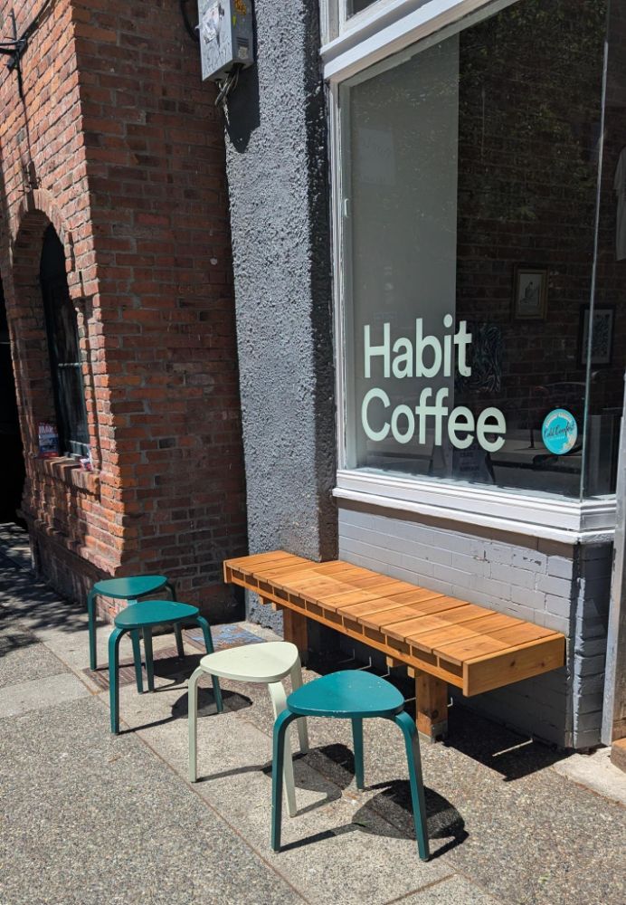 Photo of a bench and several stools in front of the window for Habit Coffee